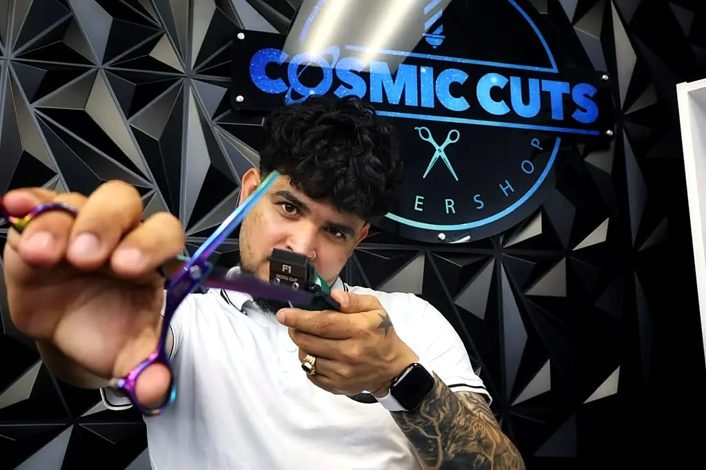Barber working with scissors in front of the Cosmic Cuts logo